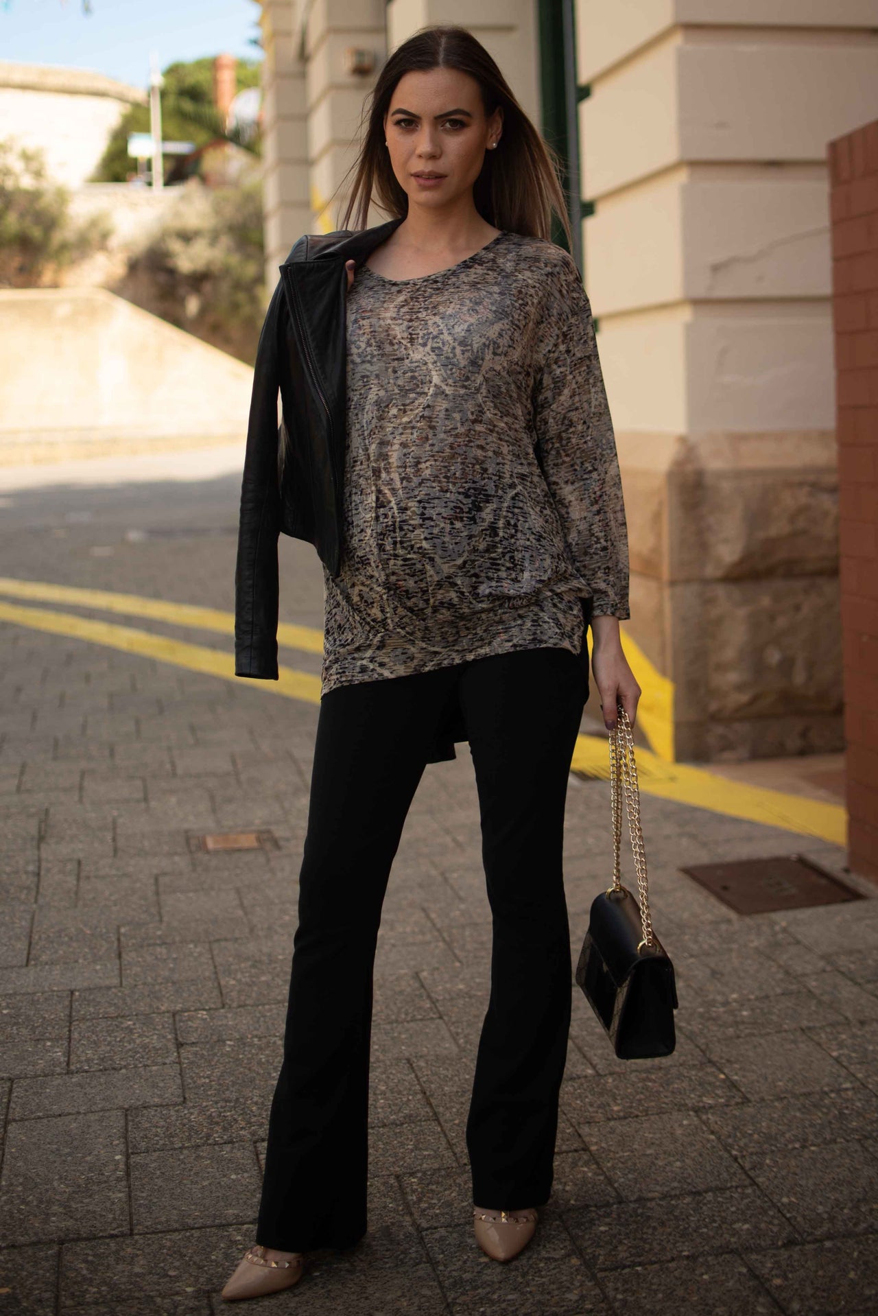 Pregnant woman standing on a street wearing a patterned top and black maternity pants.